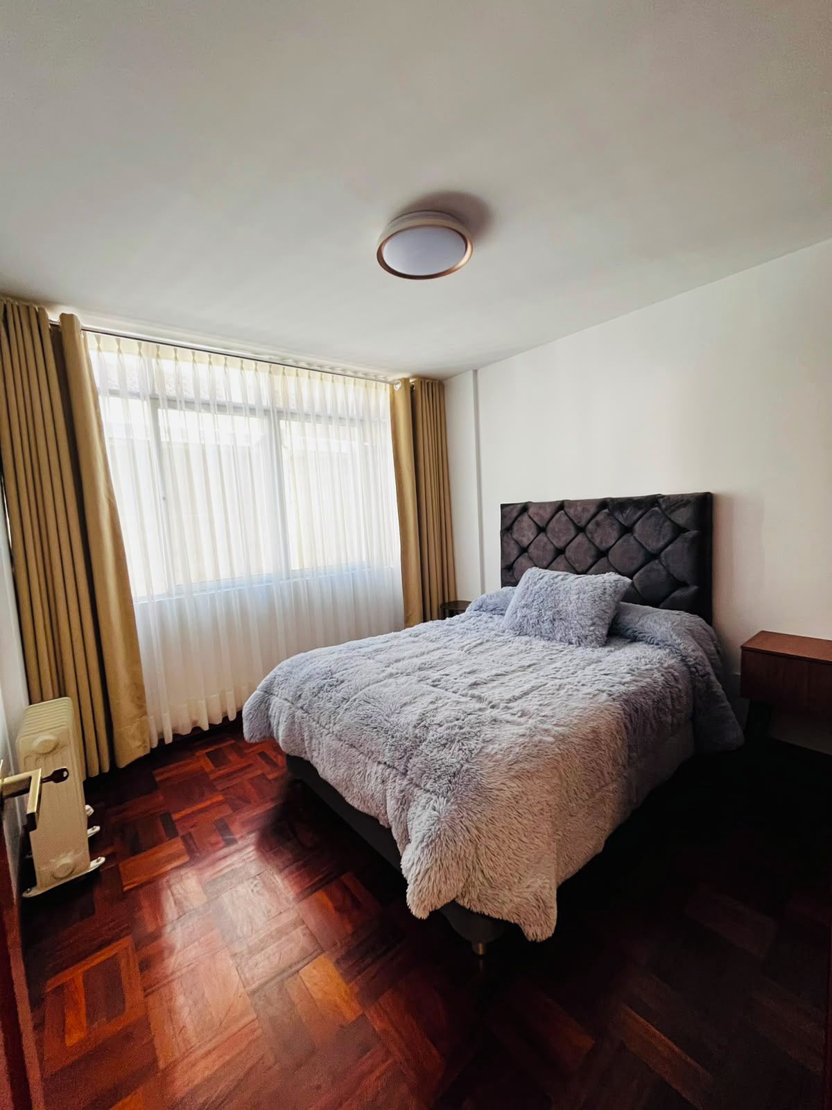 Une chambre à coucher avec un lit, un radiateur et une fenêtre avec des rideaux.