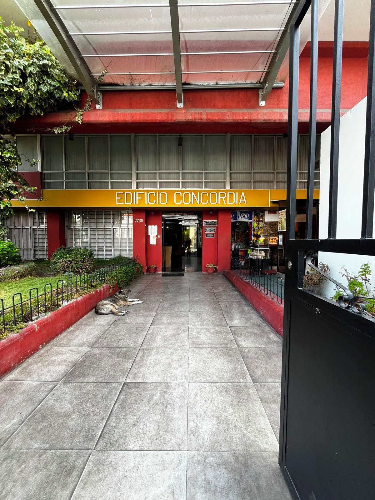 Une entrée d’immeuble avec une enseigne indiquant « EDIFICIO CONCORDIA » et un chemin pavé menant à l’entrée.