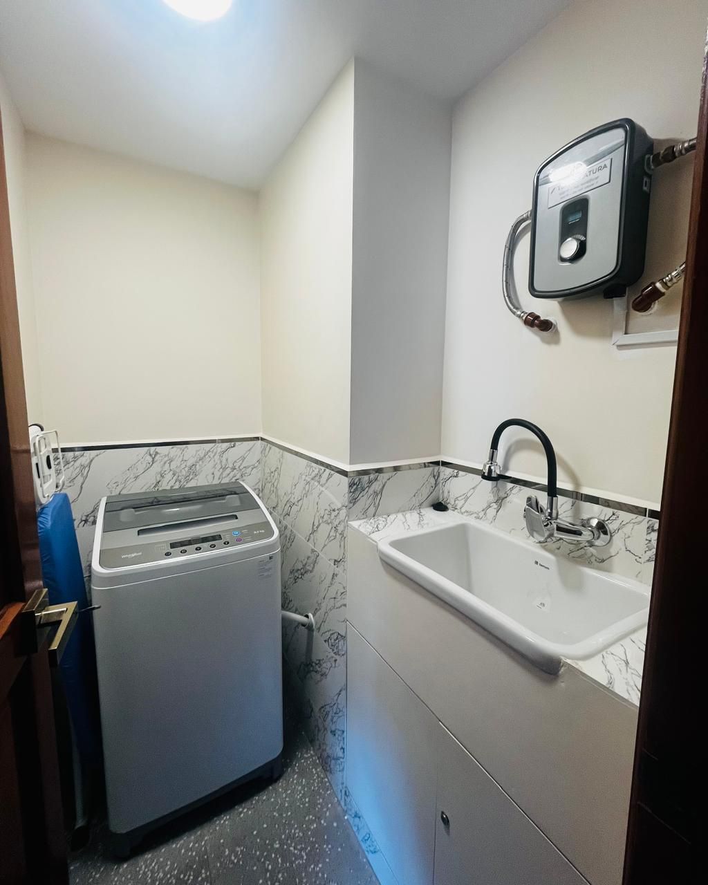 Une petite salle de bain équipée d’un lave-linge encastré, d’un lavabo et d’un radiateur fixé au mur.