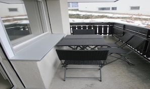 A balcony with a table and chairs, a window, and a view of a snowy landscape. - COMBINING CONTEMPORARY DESIGN WITH BREATHTAKING VIEWS OF THE ICONIC MATTERHORN (Zermatt)