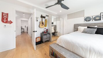 Un dormitorio con cama, una guitarra, un espejo y un ventilador de techo.