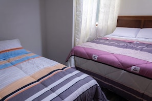 Un dormitorio con dos camas, una con cubrecama a rayas y la otra con manta acolchada.