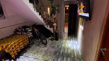 Un pasillo estrecho con una escalera que sube a un piso superior, un televisor montado en la pared y un suelo con diseño.