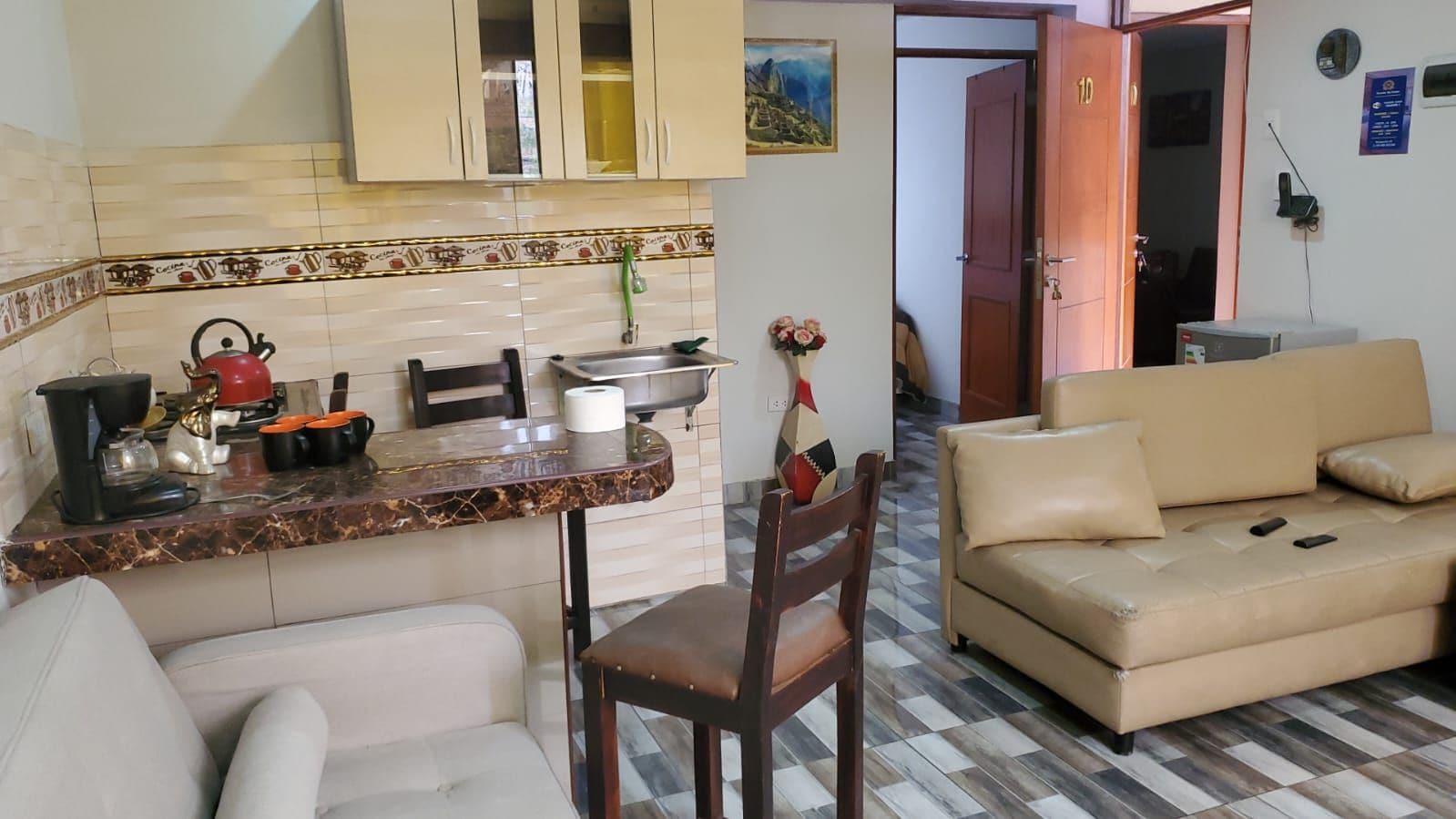 Uma sala de estar com sofá, um espaço de jantar com mesa e cadeiras, e uma cozinha com armários e bancada.