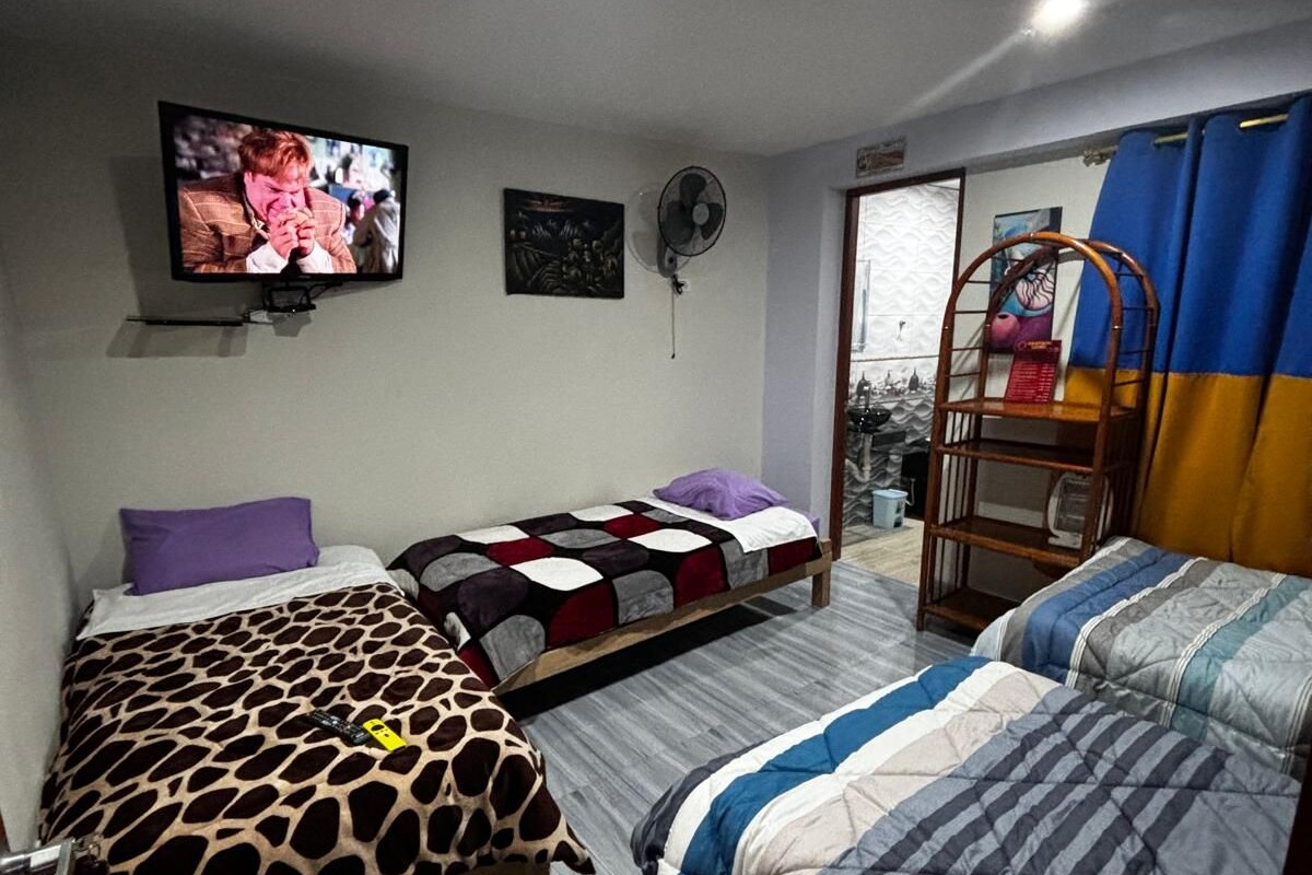 Una stanza con due letti, una televisione a parete, un ventilatore e una finestra con tende.