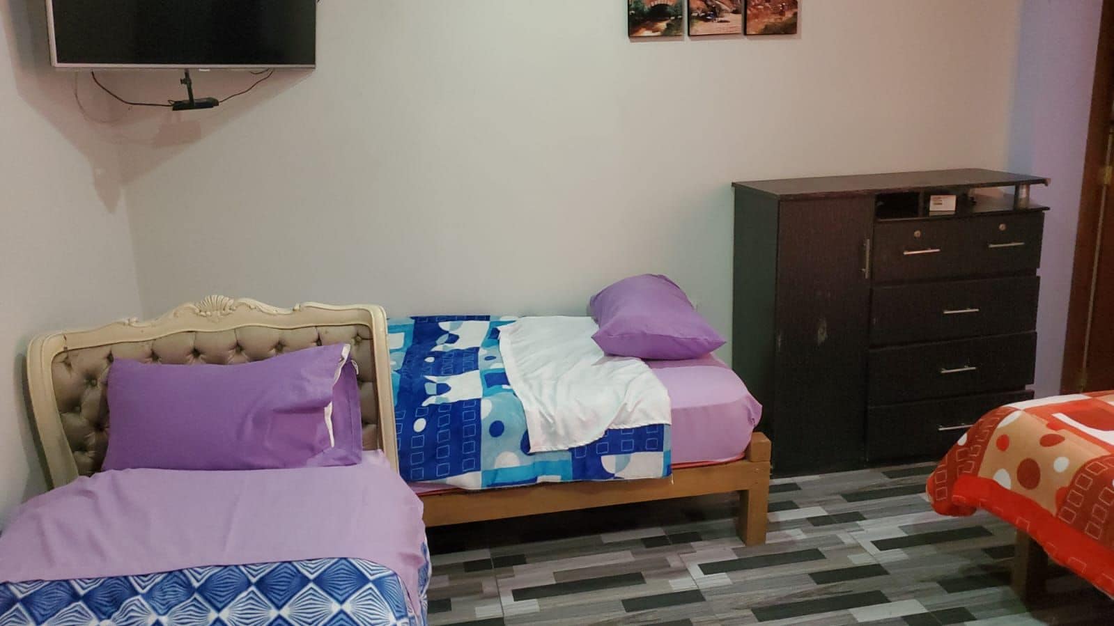 A bedroom with two beds, a wardrobe, and a television on the wall.