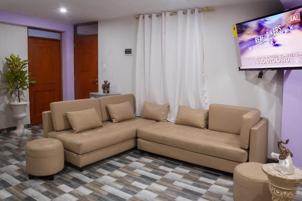 Una sala de estar con un sofá seccional color beige, un televisor montado en la pared y un piso con diseño.