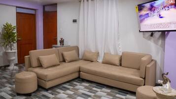 Una sala de estar con un sofá seccional color beige, un televisor montado en la pared y un piso con diseño.