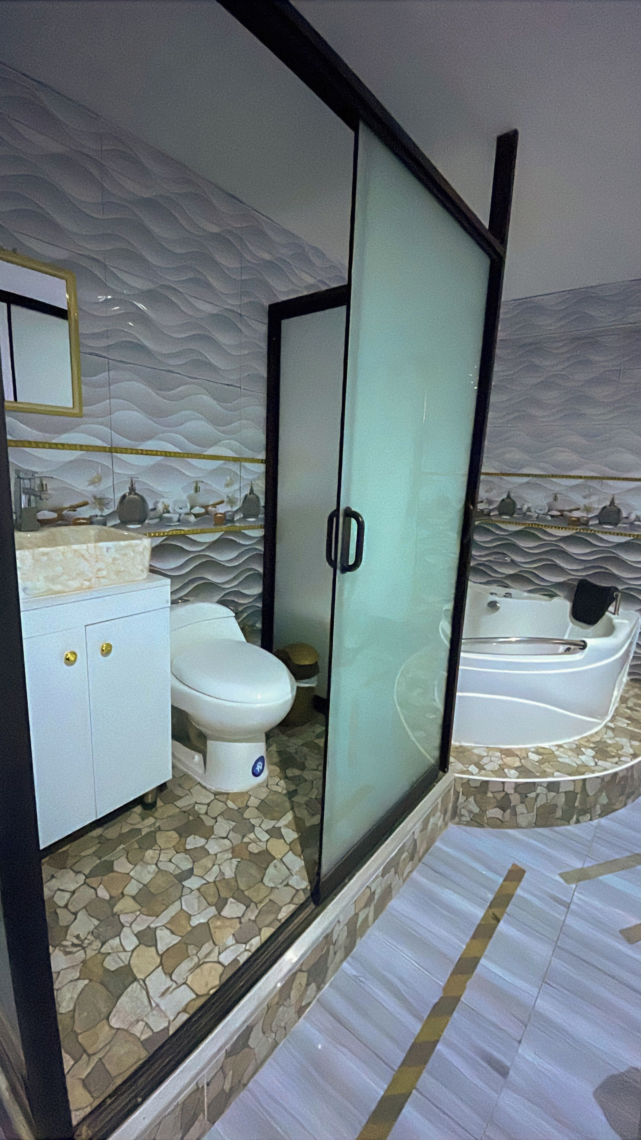A bathroom with a white toilet, a sink with gold handles, and a bathtub with a mosaic surround.
