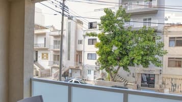 A balcony with a table and chairs, overlooking a residential area with buildings and a tree.