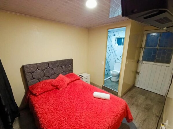 Une chambre à coucher avec un lit, une table de chevet et une salle de bain avec des toilettes, le tout accessible par une porte.