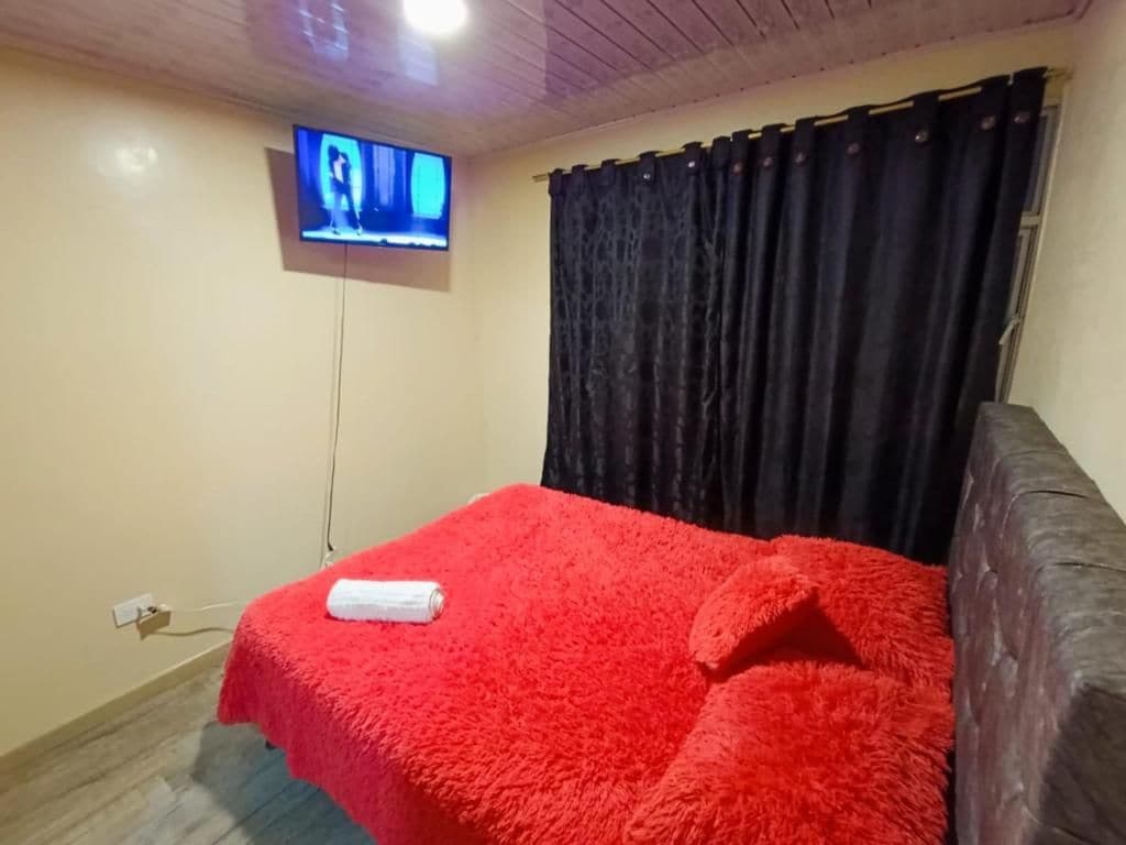 Una habitación con cama, televisor montado en la pared y ventana con cortinas.