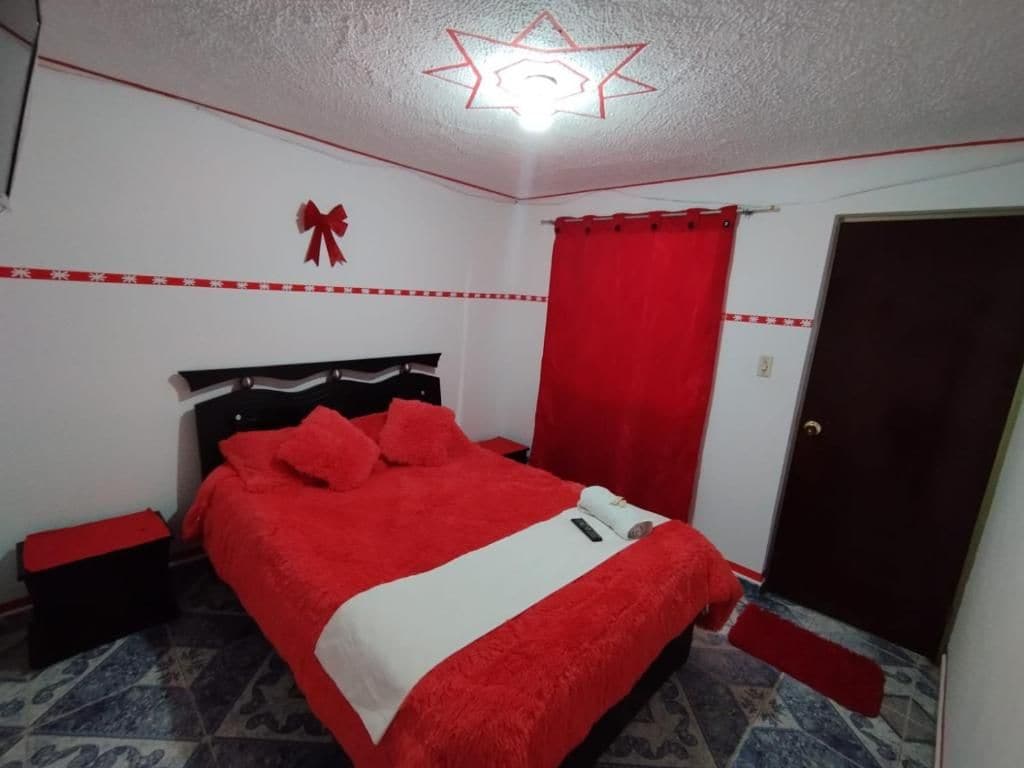 A bedroom with a bed, a nightstand, a red curtain, and a door.