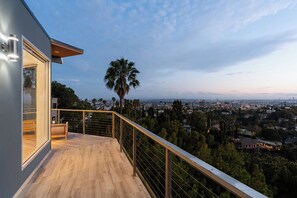 Un balcon doté d’un plancher en bois et d’une rambarde en métal, offrant une vue sur un paysage urbain avec des palmiers et des immeubles.