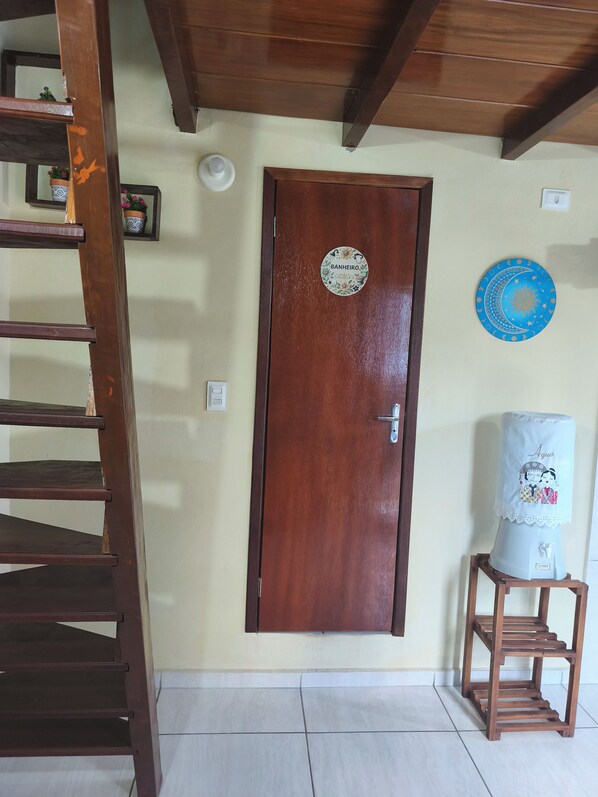 A wooden door with a circular sticker, a small shelf with a decorative item, and a wooden ladder leaning against the wall. - Cozy chalet (Cabo de Santo Agostinho)