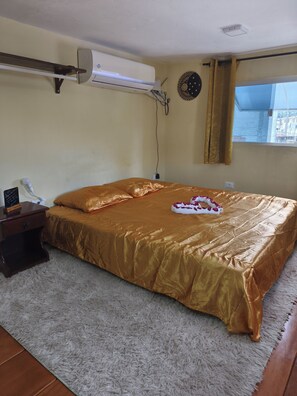A bedroom with a bed, a bedside table, a wall-mounted air conditioner, and a window with curtains. - Cozy chalet (Cabo de Santo Agostinho)