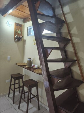 A wooden staircase with a handrail, a small table with a pitcher and cups, and two stools. - Cozy chalet (Cabo de Santo Agostinho)