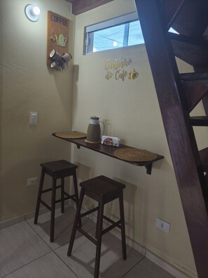 A small kitchenette with a coffee-themed decor, including a sign and a wall-mounted shelf with a coffee pot and cups. - Cozy chalet (Cabo de Santo Agostinho)