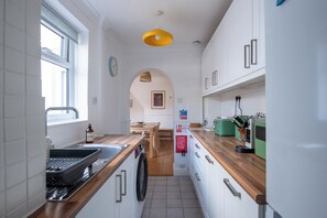 Una cocina moderna con armarios blancos, encimera de madera, una lámpara colgante amarilla y una manta anti-incendios en la pared.
