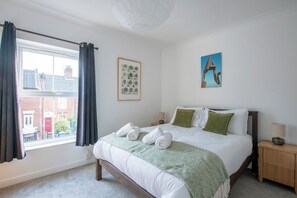 A bedroom with a bed, a window, a framed botanical print, and a painting on the wall. - Cosy & Modern | Walk To City Centre | Wood Burner (Norwich)
