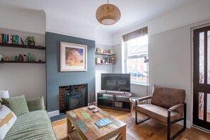 A living room with a fireplace, a television, a sofa, a coffee table, and a bookshelf. - Cosy & Modern | Walk To City Centre | Wood Burner (Norwich)