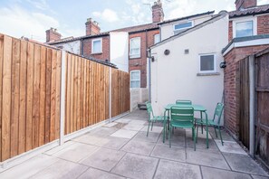 Un área de patio con cerramiento de madera, una pared blanca y una ventana pequeña.