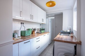 Eine moderne Küche mit weißen Schränken, einer Holz Arbeitsplatte und einer gelben Pendelleuchte.