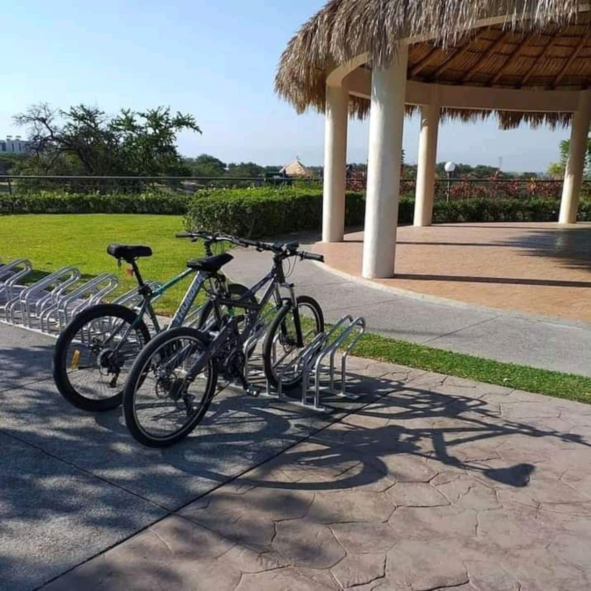 A covered pavilion with a thatched roof, a bicycle parking area with a rack, and a paved walkway.