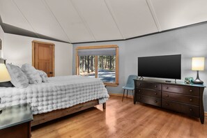 A bedroom with a bed, a dresser, a television, and a window with a view of trees. - Riverfront Ski Cabin W/ Hot Tub & Dock! (Bend)