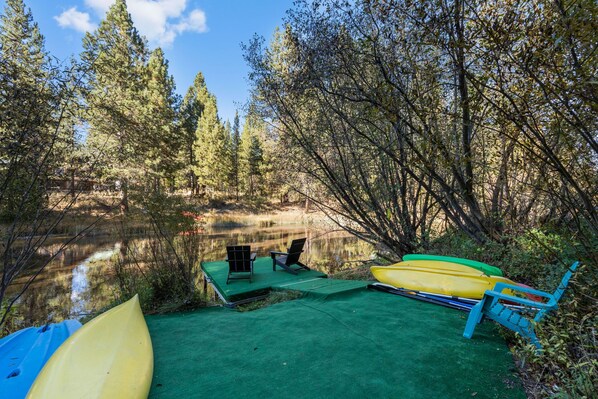 A campsite with a green mat, two chairs, and two kayaks. - Riverfront Ski Cabin W/ Hot Tub & Dock! (Bend)