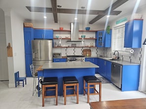A modern kitchen with blue cabinets, stainless steel appliances, and a central island with stools.