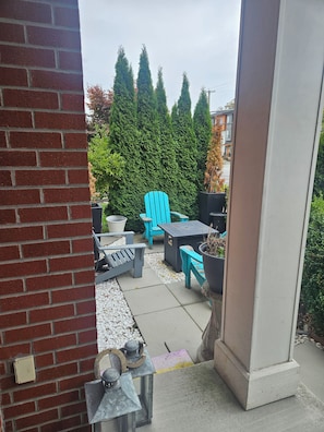 An outdoor patio with a brick wall, a blue Adirondack chair, a table, and a potted plant.
