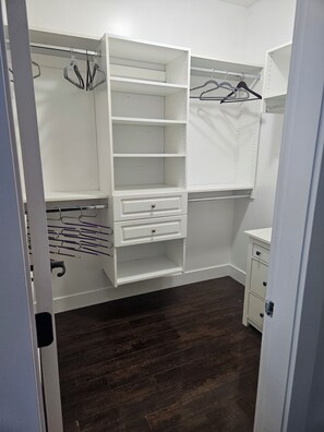 Un dressing avec des étagères ouvertes, une tringle pour suspendre les vêtements et une petite commode.