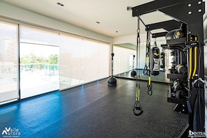 Ein Fitnessstudio mit Trainingsgeräten, großen Fenstern und einem blauen Boden.