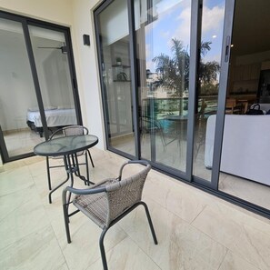 Ein Balkon mit Glastür, einem kleinen Tisch und einem Korbstuhl.