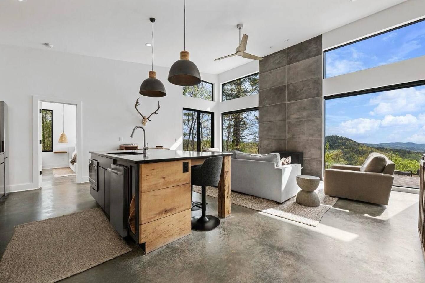 Una cocina moderna con una isla central, una zona de comedor con un sofá y ventanas amplias que ofrecen vistas al exterior.