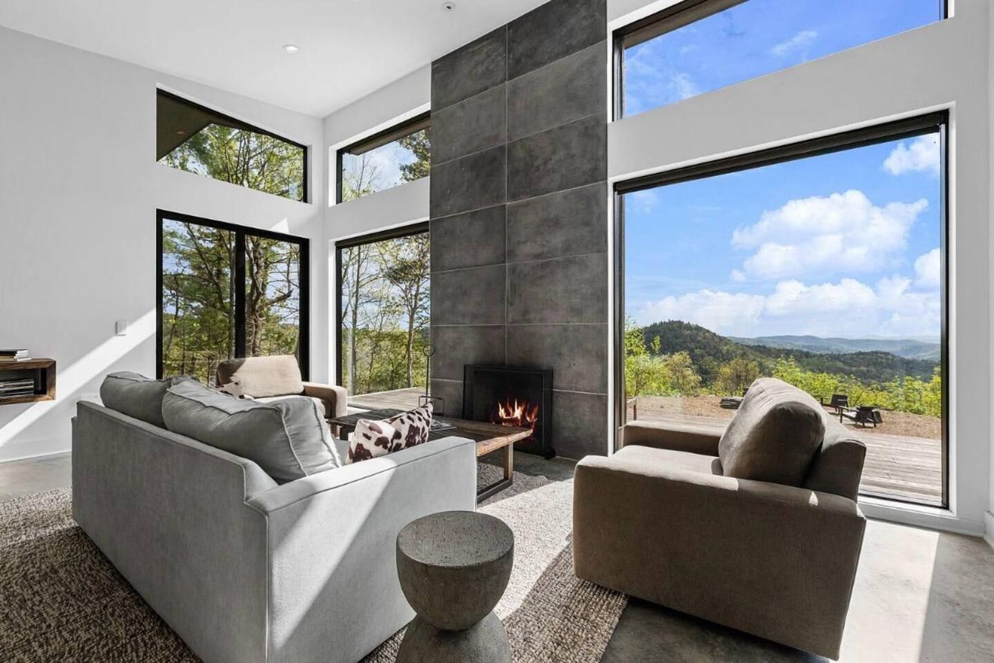 A modern living room with a fireplace, large windows, and a view of the outdoors.