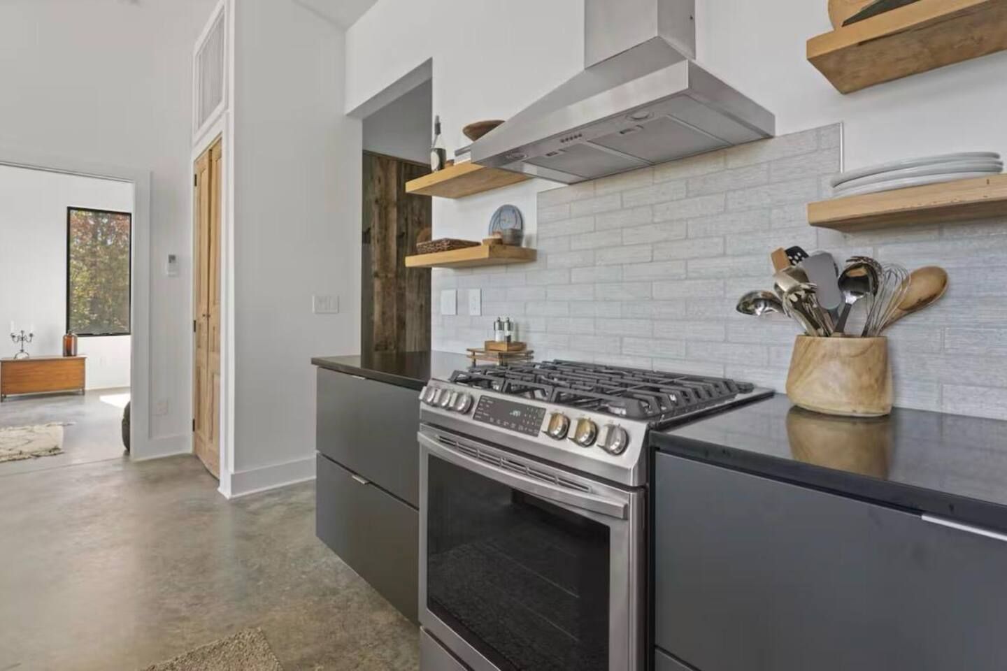 A modern kitchen with a gas stove, oven, and wooden shelves above.