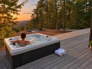 Ein Whirlpool auf einer Holzdielen-Terrasse mit Blick auf Bäume und einen Sonnenuntergang.