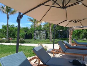 Un espace de détente aménagé sur la plage, avec des chaises longues et un grand parasol pour offrir de l’ombre.