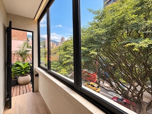 Ein Zimmer mit großem Fenster, Blumentopf und Blick auf die Straße sowie umliegende Gebäude.