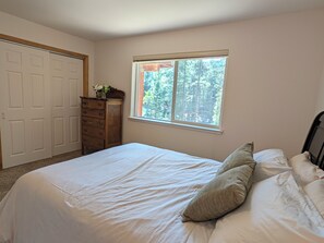 Ein Schlafzimmer mit Bett, Schminktisch, Fenster und Blick auf Bäume.