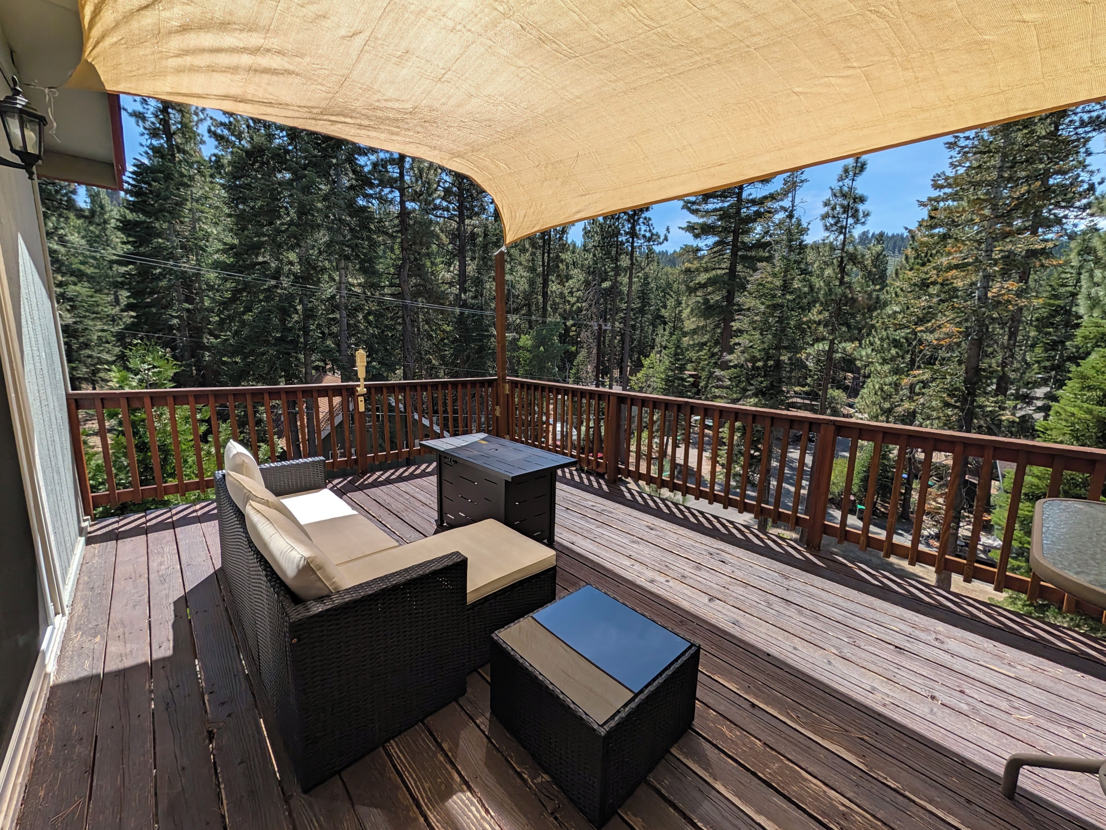 Una terraza de madera con mobiliario exterior, una pérgola y vista a un bosque.