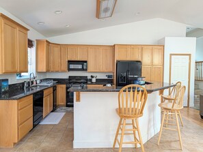 Una cucina moderna con mobili in legno, un frigorifero nero, un forno a microonde e un piano cottura. Ci sono due sedie in legno al bancone.