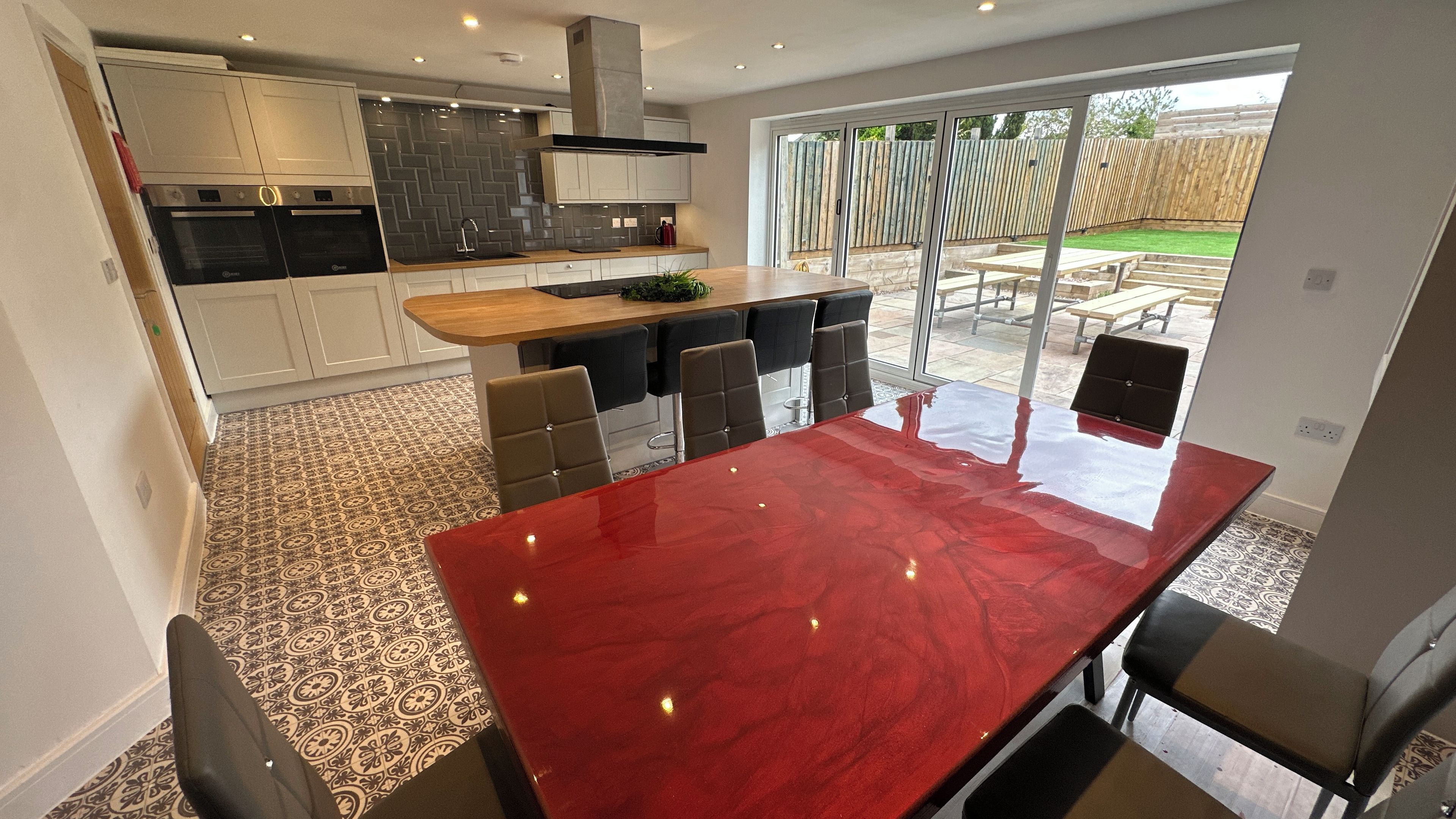 Une cuisine moderne dotée d’un plan de travail en marbre rouge, d’un four encastré et d’un grand espace à manger avec une porte vitrée donnant sur une terrasse extérieure.