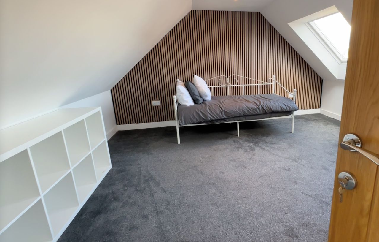 Une chambre à coucher aménagée dans un espace en hauteur, avec un plafond en pente, un lit superposé, un puits de lumière et des étagères intégrées.
