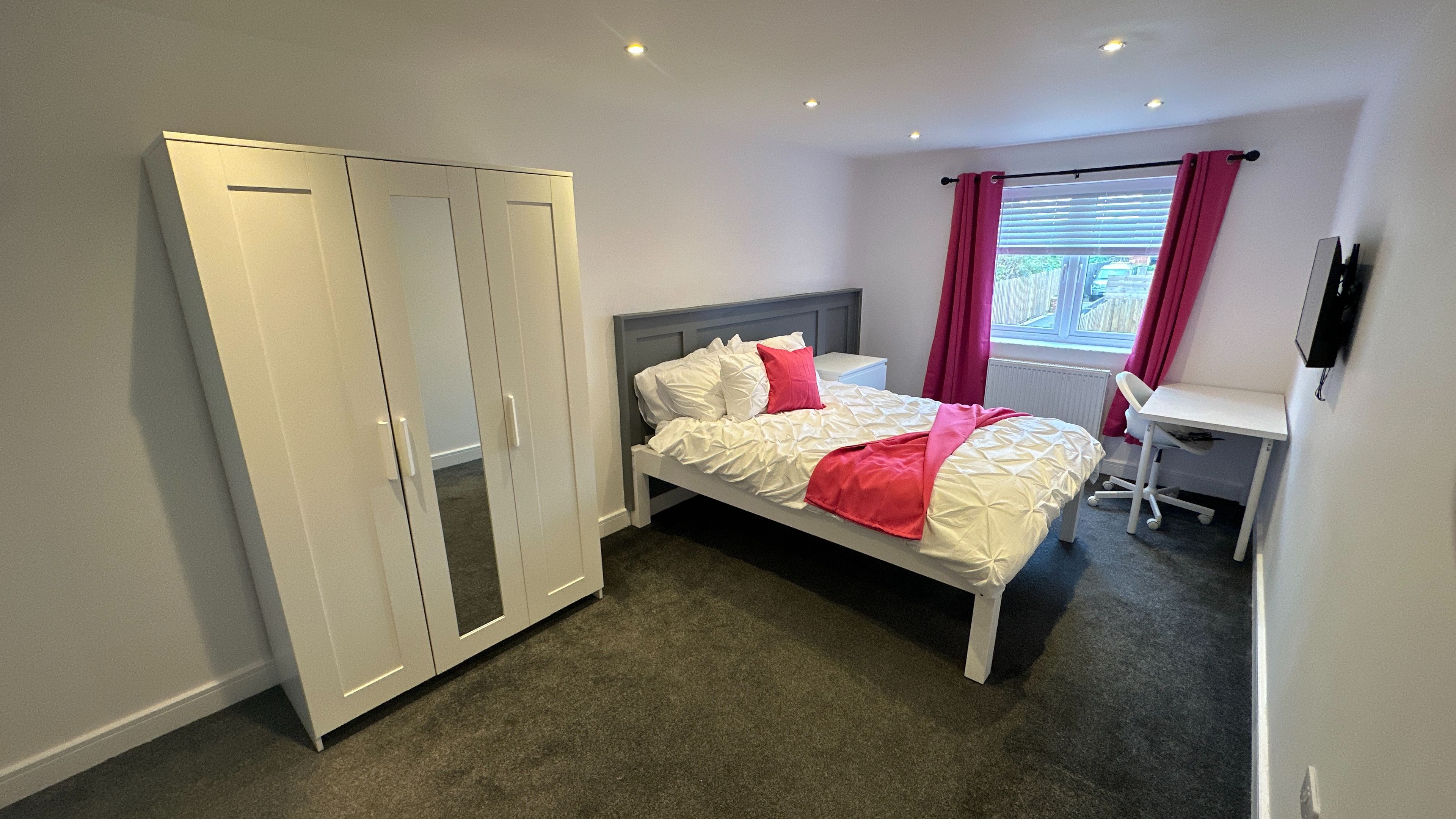 A bedroom with a bed, a desk, and a wardrobe.