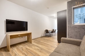 A modern living room with a flat-screen TV, a wooden console table, a grey sofa, and a dining area with chairs. - Chic 1BR Apartment in Pietà with Balcony (Tal-Pietà)