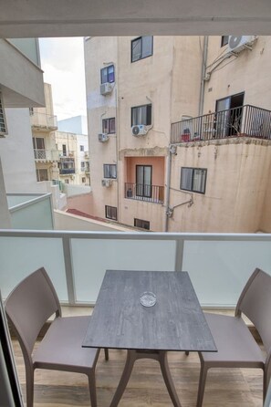 A balcony with a table and chairs, overlooking a building with multiple windows and balconies. - Calm 1BR Apartment in Pietà with Balcony (Tal-Pietà)