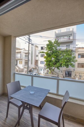 A balcony with a table and chairs, overlooking a residential area with buildings and a tree. - Airy 1BR Apartment in Pietà with Balcony (Tal-Pietà)